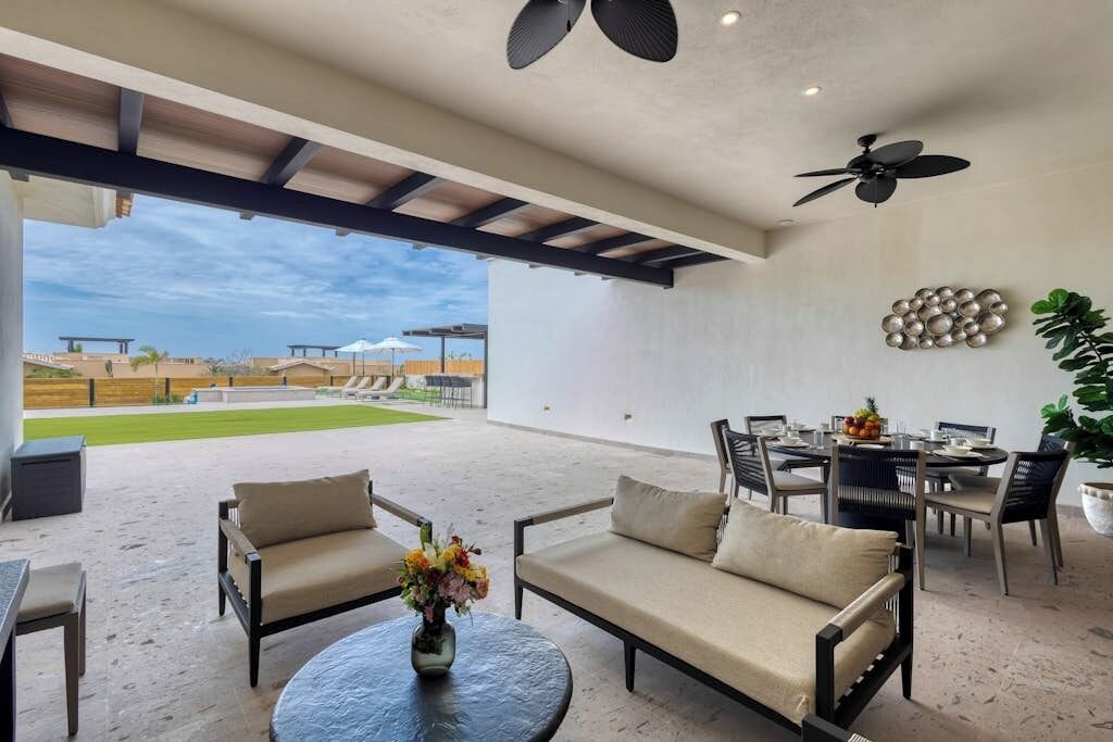 Un amplio patio con mobiliario exterior, zona de comedor y vista a un campo deportivo.