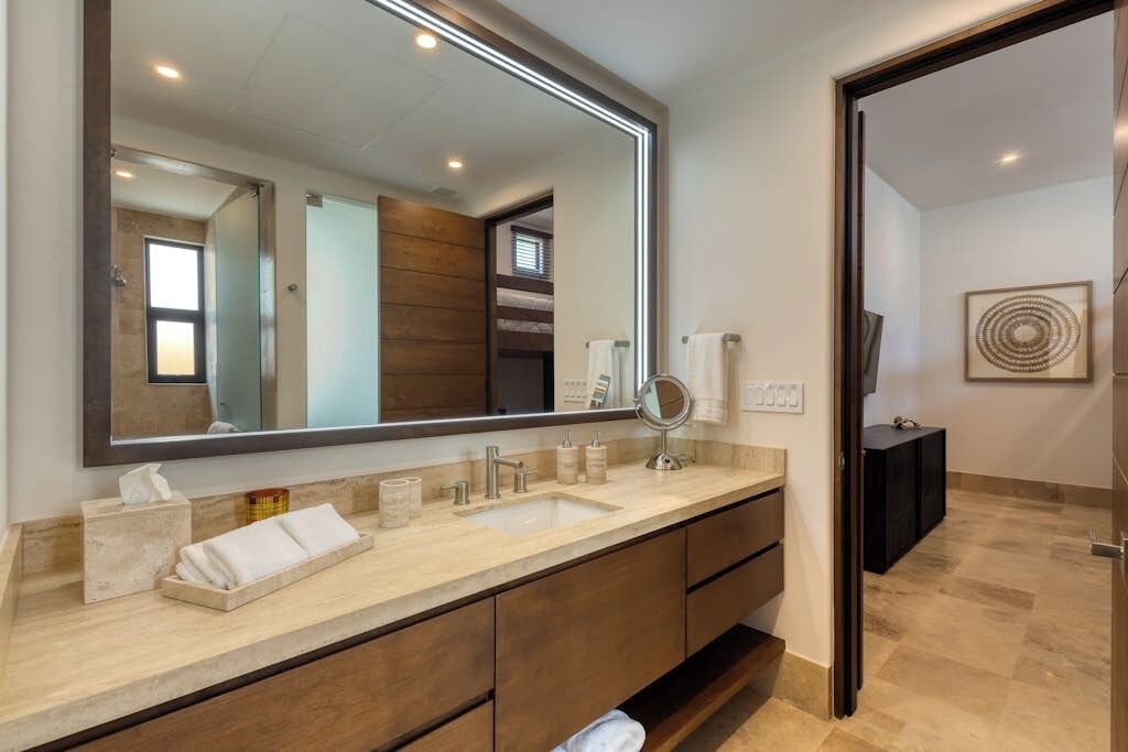 A modern bathroom with a large mirror, a sink, and a vanity with drawers.