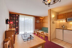 Um quarto acolhedor com uma mesa de jantar de madeira, cadeiras, um sofá, uma cozinha compacta com micro-ondas e uma janela com cortinas.