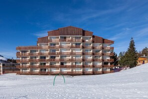 Um hotel com várias andares e varandas, uma pista de esqui em primeiro plano, e um céu azul límpido.