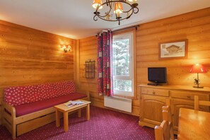 Interior d'una cabana de fusta amb un sofà, taula, televisió i finestra amb cortines.