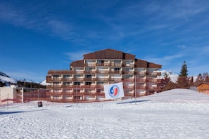 Ett hotell med flera våningar och modern design, med balkonger och en skidbacke som syns i bakgrunden.