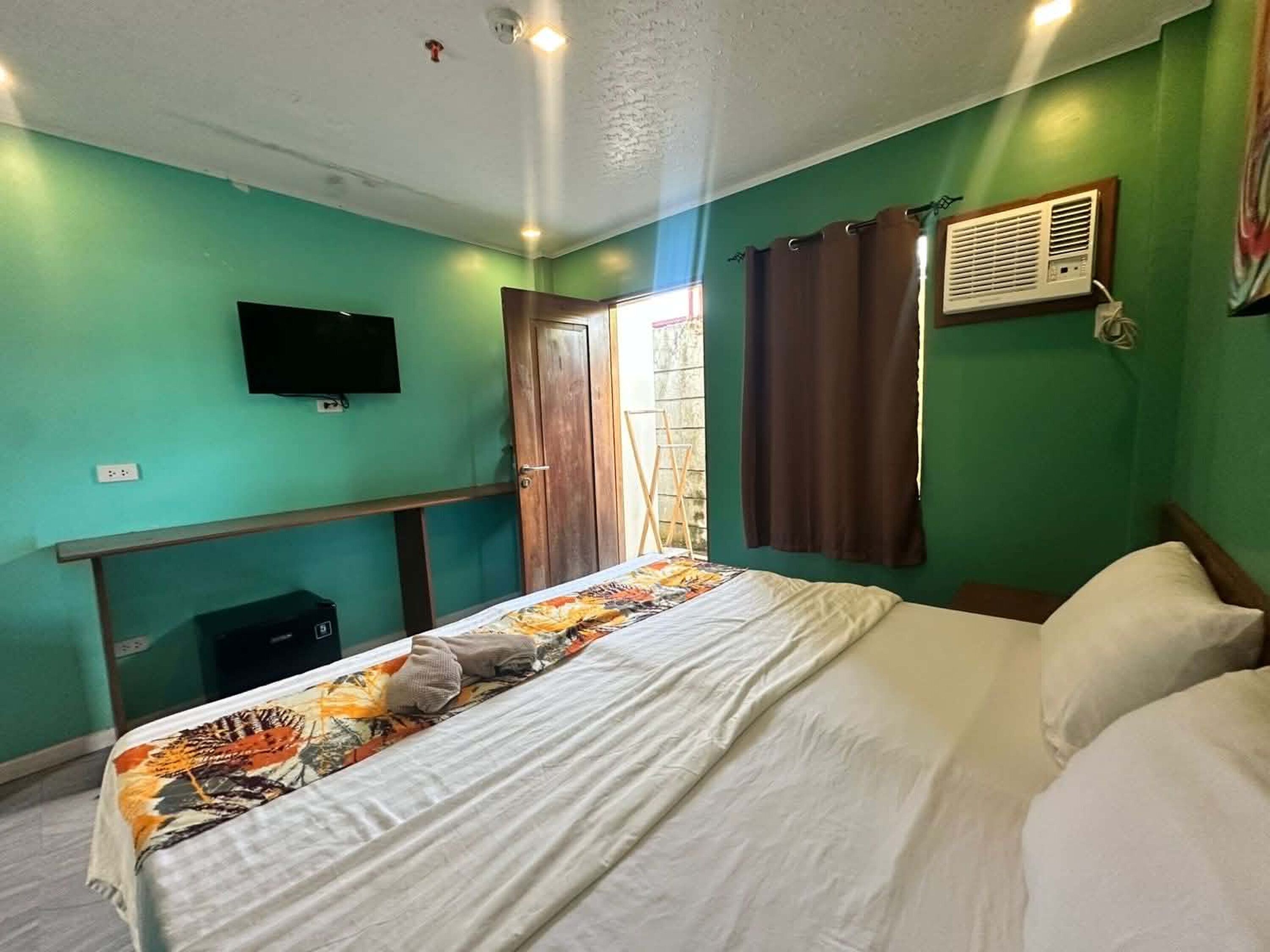 Quarto com cama, televisão na parede, janela com cortinas e ar condicionado.