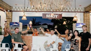 En grupp människor sitter vid en bardisk, och ovanför finns en skylt med texten ”MAOY”.
