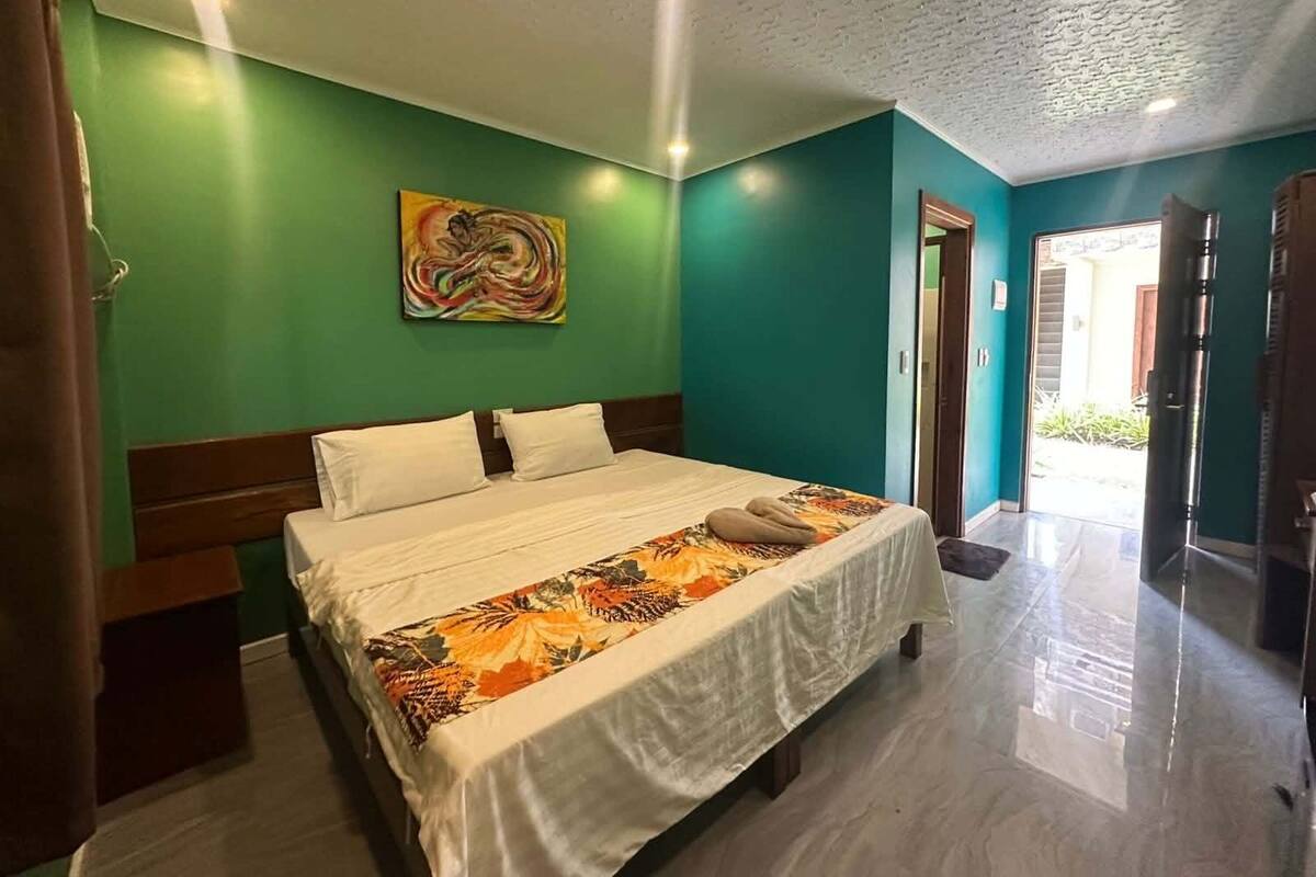A room with a bed, a painting on the wall, and a door leading to another room.