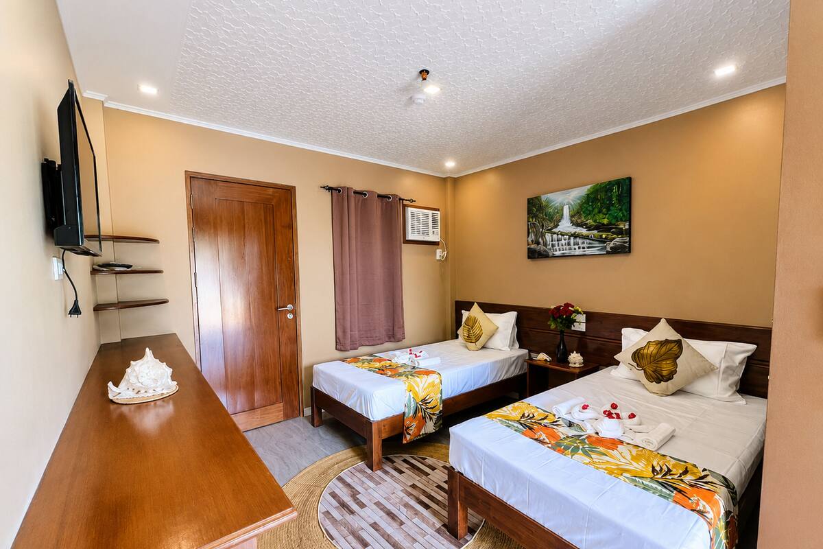 A hotel room with two beds, a desk, a TV, and a painting on the wall.