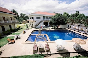 A swimming pool with lounge chairs and a gazebo, surrounded by a well-maintained lawn and a building with a red roof. - Palette Lifestyle Pangnao Resort Bohol (Panglao)
