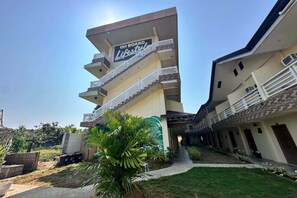 Un hôtel à plusieurs étages doté de balcons, d’une enseigne indiquant « ON BOARD Lifestyle », et d’un jardin bien entretenu.