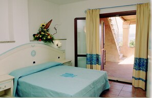 A bedroom with a bed, bedside table, lamp, and a flower arrangement. - Le Corti Di Marinella 6p Sea View (Marinella)