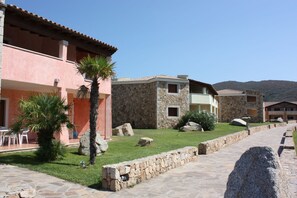 A courtyard with stone buildings, a palm tree, and a stone pathway. - Le Corti Di Marinella 6p Garden View (Marinella)