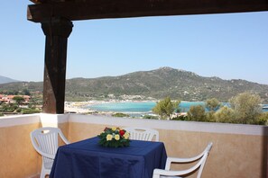 A balcony with a table and chairs, overlooking a beach and mountains. - Le Corti Di Marinella 4p Sea View (Marinella)