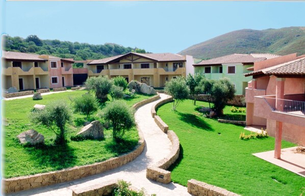 A courtyard with a curved pathway, stone walls, and greenery. - Le Corti Di Marinella 4p Sea View (Marinella)