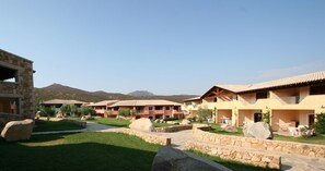 A resort with multiple buildings, stone pathways, and a mountainous backdrop. - Le Corti Di Marinella 4p Garden View (Marinella)