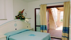 A bedroom with a bed, bedside table, lamp, and a flower arrangement. - Le Corti Di Marinella 4p Garden View (Marinella)