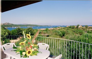 A balcony with a table set for dining, overlooking a coastal landscape with greenery and a view of the sea. - Le Corti Di Marinella 4p Garden View (Marinella)