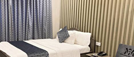 Una habitación de hotel con cama, mesita de noche, teléfono, control remoto, almohada y cortinas.