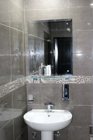 Une salle de bain avec un lavabo blanc, un miroir en verre et une porte noire.