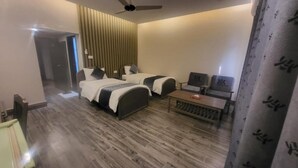 A hotel room with two beds, a desk, a chair, a ceiling fan, and a window with curtains. - Hotel Akbar International (Rawalpindi)