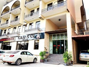 A multi-story building with balconies, a restaurant named 'GHAI & GO,' and parked cars.