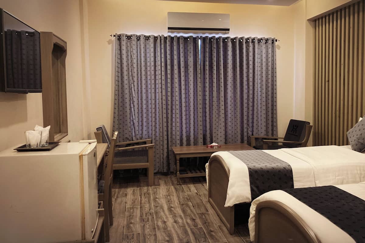 Habitación de hotel con dos camas, un escritorio, una silla, una mesita con una caja de pañuelos y un televisor montado en la pared.