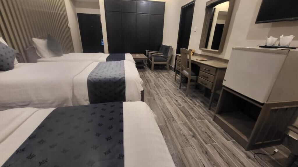 A hotel room with two beds, a desk, a chair, a mirror, and a television.