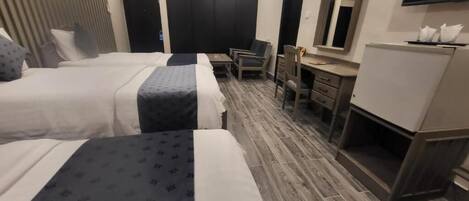 A hotel room with two beds, a desk, a chair, a mirror, and a television.