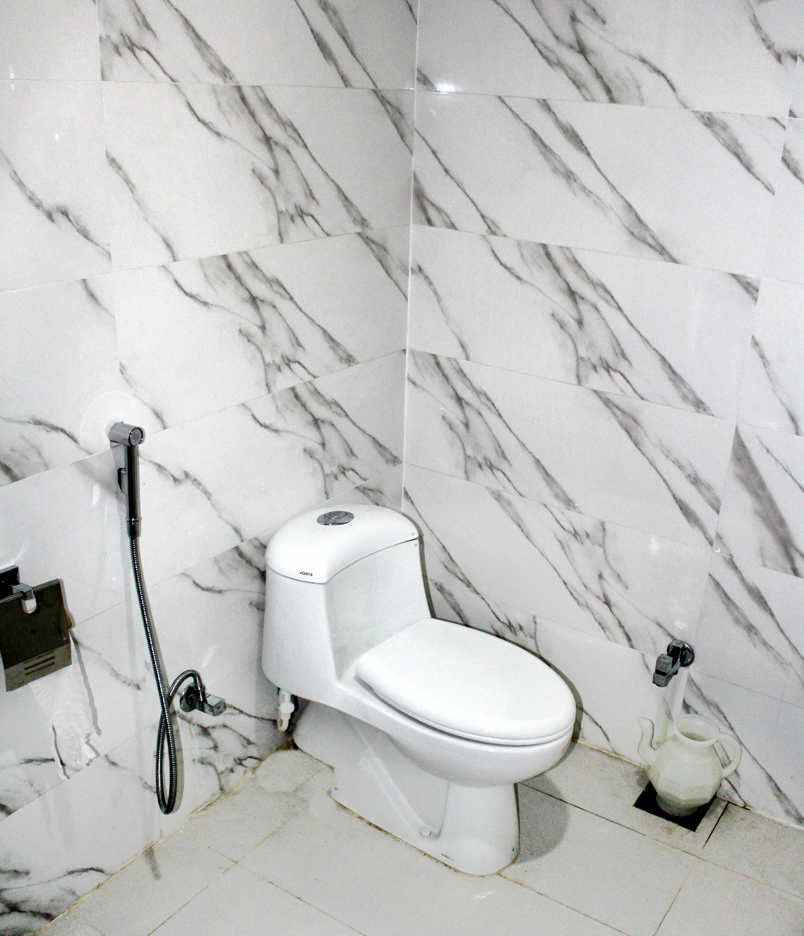 A bathroom with a white toilet, a handheld showerhead, and a marble-patterned wall.