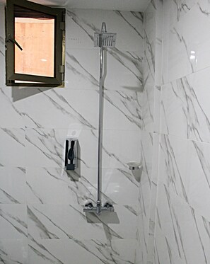 A bathroom with a shower, marble walls, and a window.