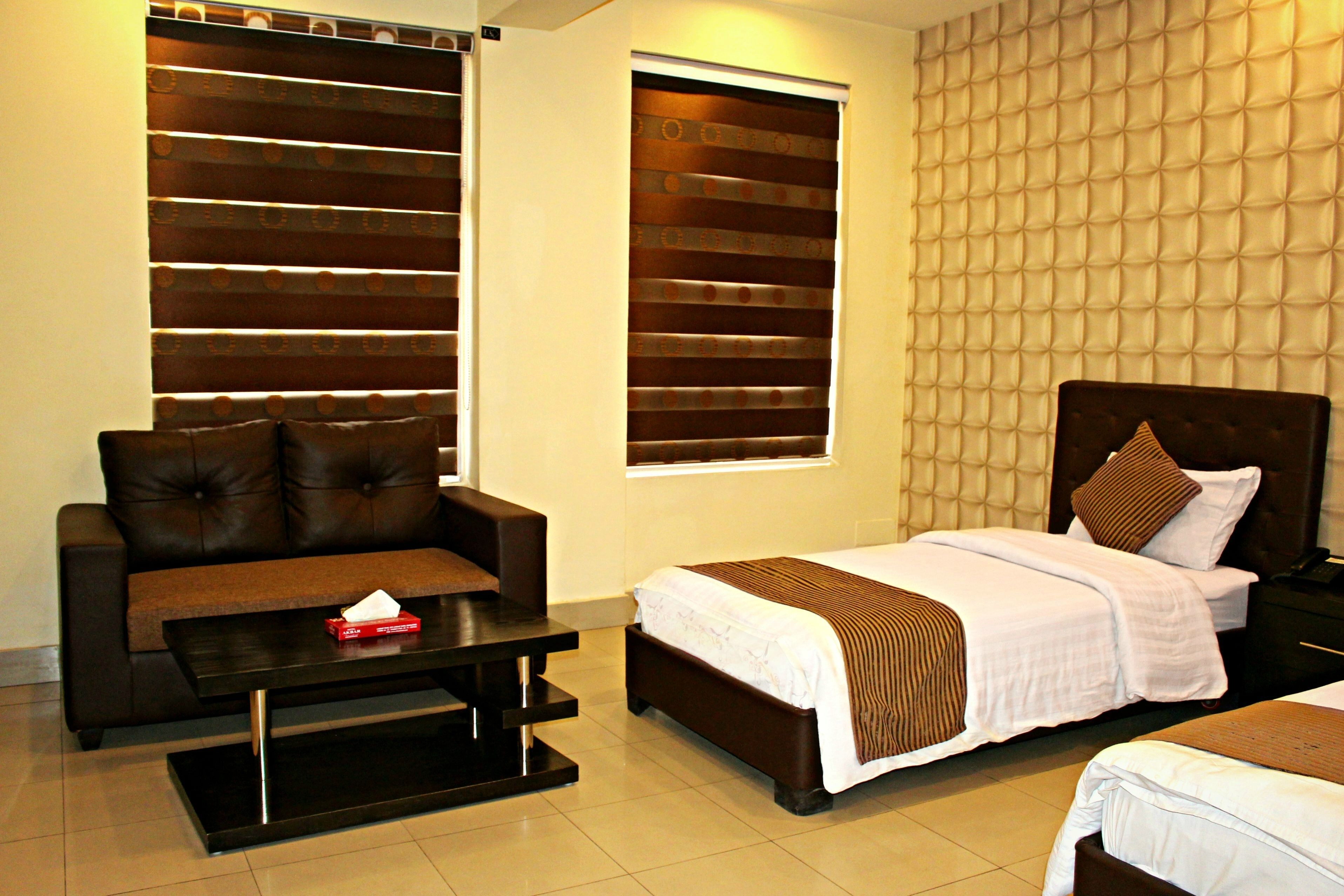 A hotel room with a bed, a sofa, a table, and a window with blinds.