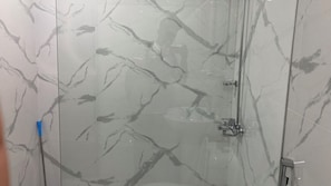 Une douche entiĂšrementClose avec des parois en verre et un mur dĂ©corĂ© dâun motif imitant le marbre.