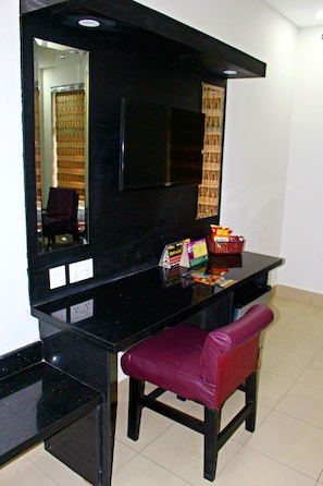 A room with a black desk, a mirror, a television, a red chair, and a basket with snacks. - Hotel Akbar International (Rawalpindi)