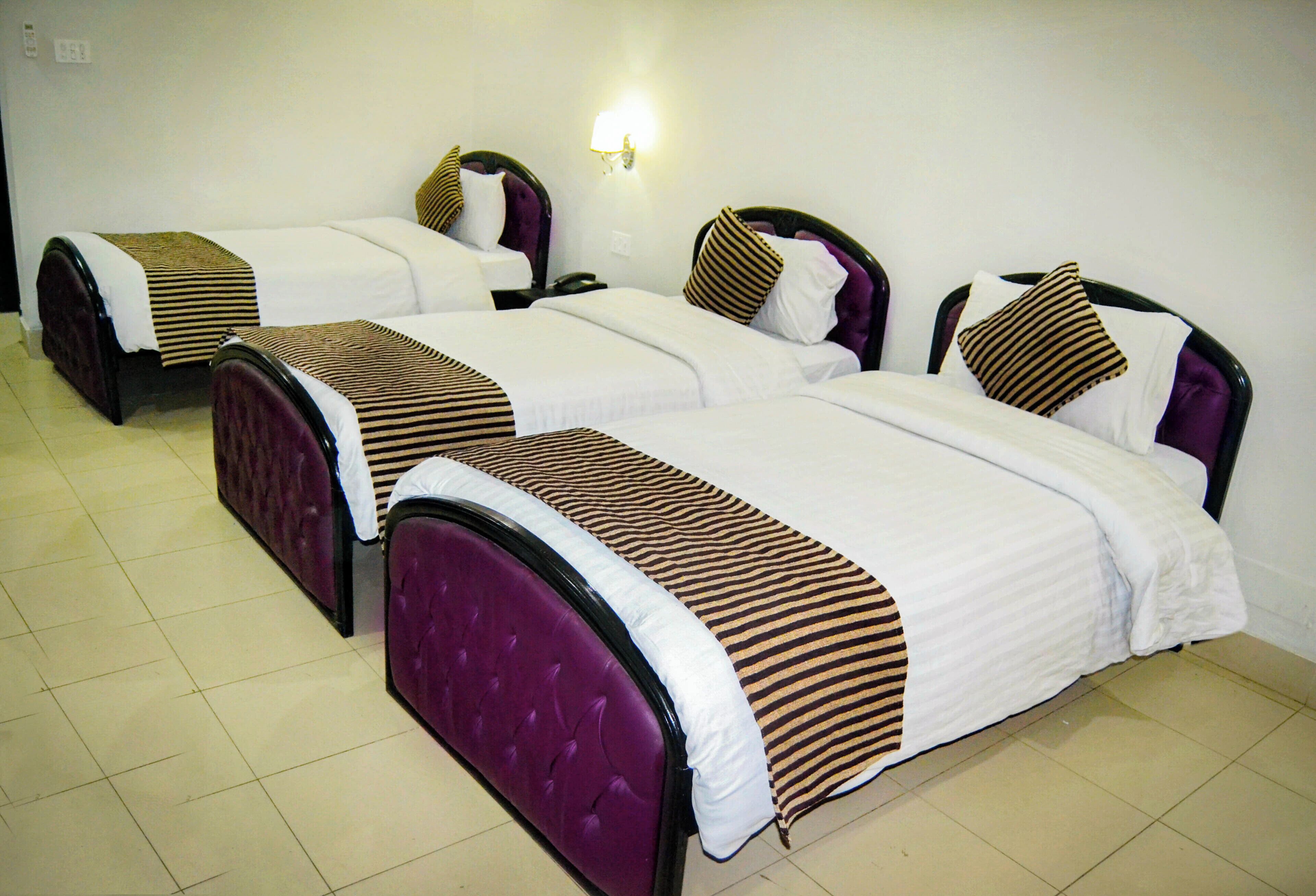 A hotel room with three beds, each with a headboard and a bedside table.
