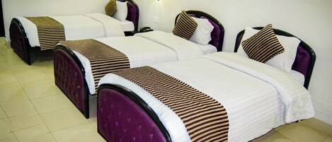 A hotel room with three beds, each with a headboard and a bedside table.