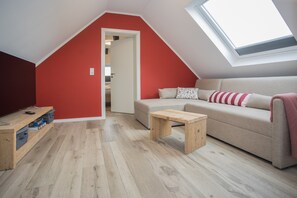 A room with a sloped ceiling, a red wall, a beige sofa, a wooden coffee table, and a skylight. - Appartement - Winterbergerstrasse 3, nr. 511 | Neuastenberg (Winterberg)