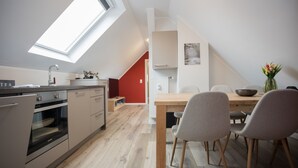 A modern kitchen with a skylight, a dining area with a wooden table and chairs, and a red accent wall. - Appartement - Winterbergerstrasse 3, nr. 511 | Neuastenberg (Winterberg)