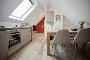 A modern kitchen with a skylight, a dining area with a wooden table and chairs, and a red accent wall. - Appartement - Winterbergerstrasse 3, nr. 511 | Neuastenberg (Winterberg)