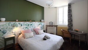 A bedroom with a bed, a nightstand, a chair, a table, a fireplace, and a window with curtains. - ATELIER CHARNOZ, heritage and Parodian ceramics (Paray-le-Monial)