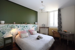 Une chambre à coucher comprenant un lit, une table de chevet, une chaise, une table, une cheminée et une fenêtre avec des rideaux.