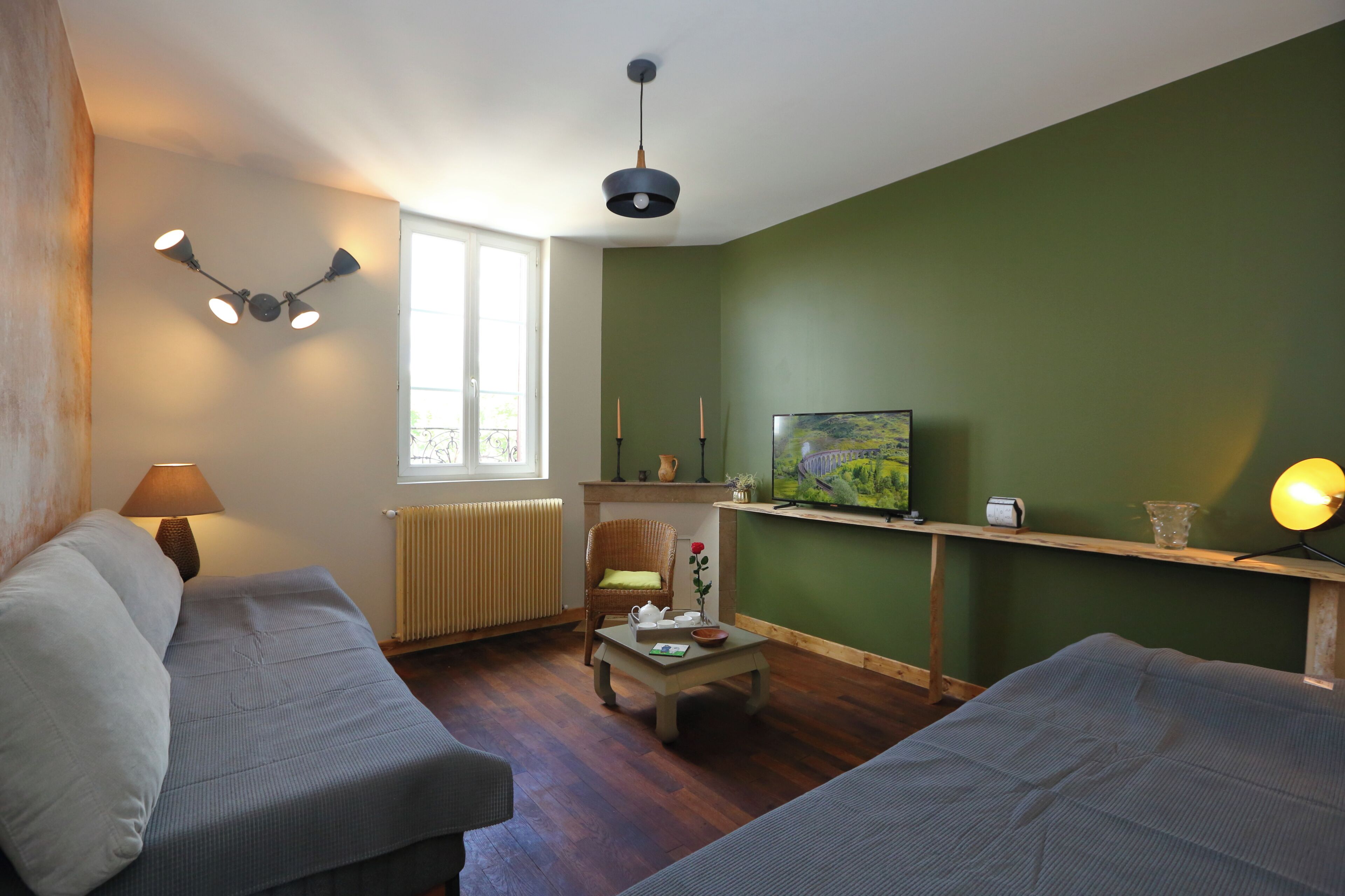 Una sala de estar con dos sofás, una mesa de centro, un televisor sobre un mueble, una lámpara y una ventana con vistas.
