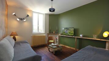 Una sala de estar con dos sofás, una mesa de centro, un televisor sobre un mueble, una lámpara y una ventana con vistas.