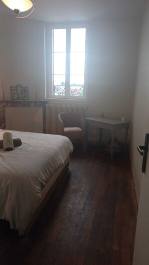 Quarto com cama, cadeira, mesa pequena, radiador e janela.