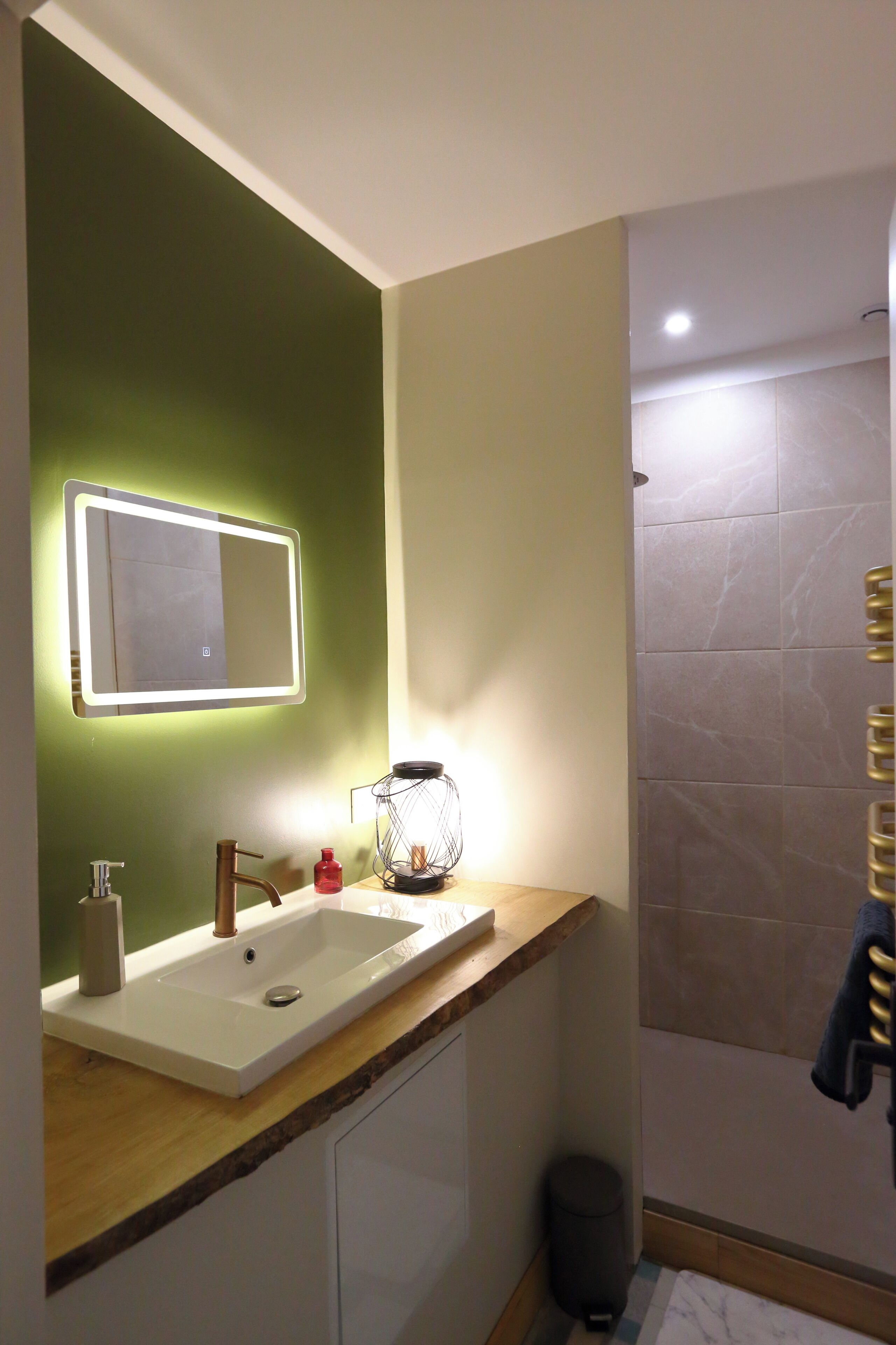 Un baño con lavamanos blanco, espejo con iluminación, toallero y zona de ducha.