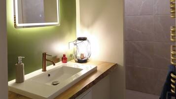 Un baño con lavamanos blanco, espejo con iluminación, toallero y zona de ducha.
