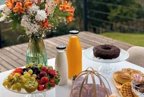 Une table avec un assortiment de fruits, une bouteille de jus d’orange, un gâteau au chocolat et des pâtisseries.
