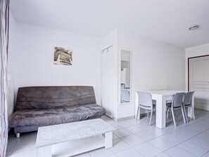 A modern room with a grey sofa, a small white table, and a dining area with chairs. - Les Demeures de la Massane M38C (Argeles-sur-Mer)