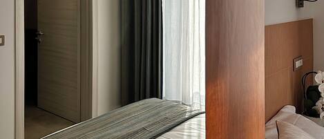 A hotel room with a bed, a wooden headboard, a bedside table with a lamp, and a door leading to another room.