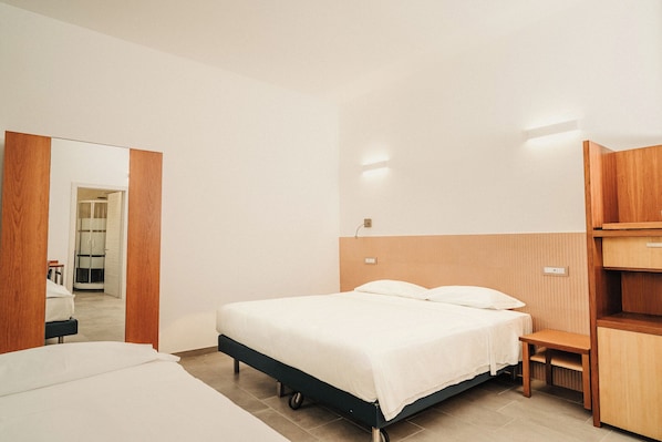 A hotel room with a bed, a wooden nightstand, a mirror, and a door leading to a bathroom.