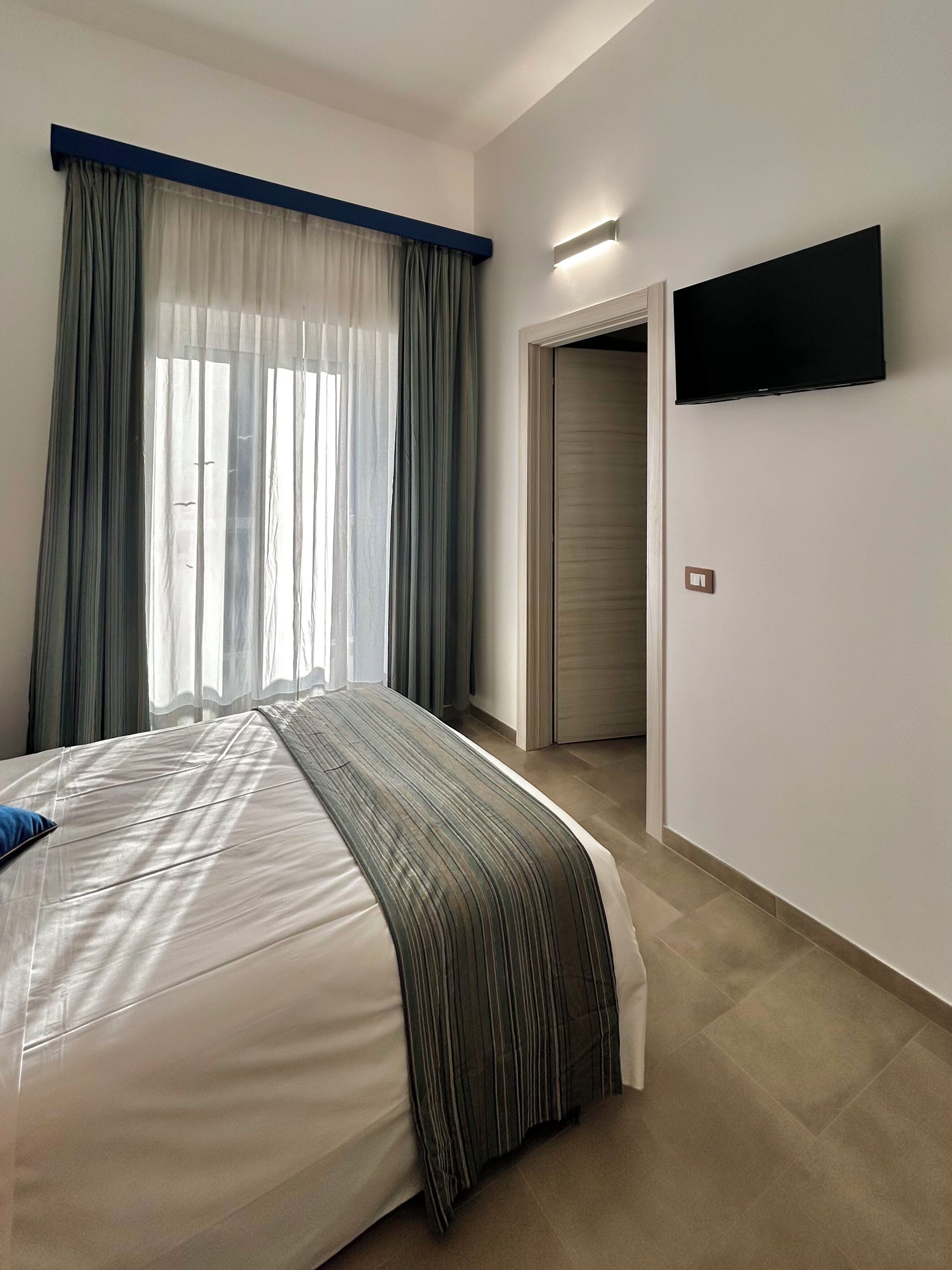 Een slaapkamer met een bed, gordijnen, een televisie en een deur.