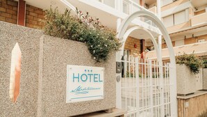 A hotel entrance with a sign, a gated entrance, and a building with balconies. - Hotel Mediterraneo (Santa Marinella)