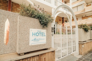 A hotel entrance with a sign, a gated entrance, and a building with balconies.